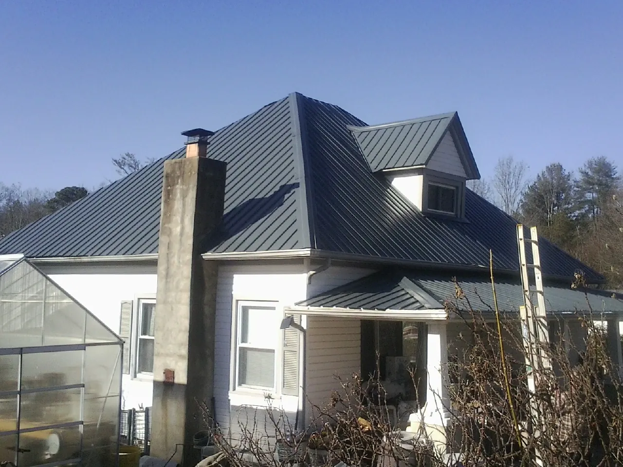 Dark blue standing seam metal roof on a white farmhouse with dormer — Slate & Tile Roof Repair by Roofing Brothers in Slickville