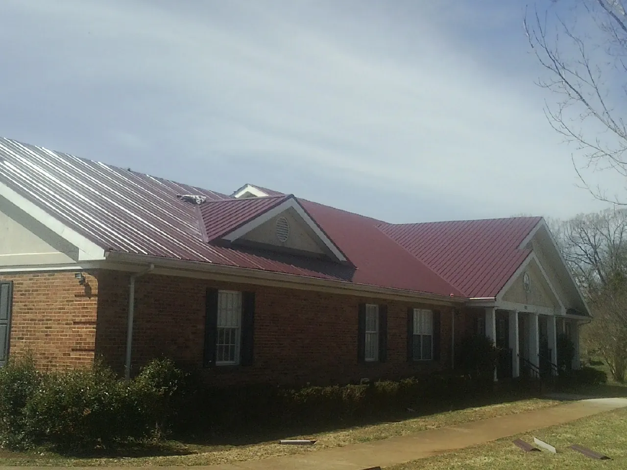 Red metal roof with gabled entries on a long brick building, from a Hail Damage Roof Repair job in Slickville