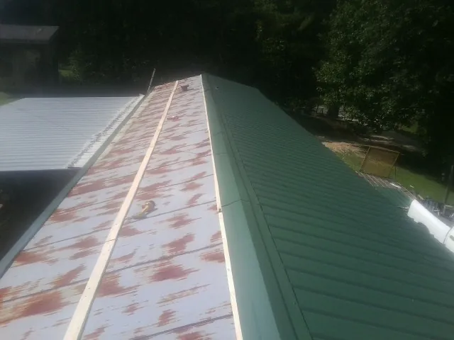 Old rusted panels beside newly installed green metal roofing — Wind Damage Roof Repair by Roofing Brothers in Slickville