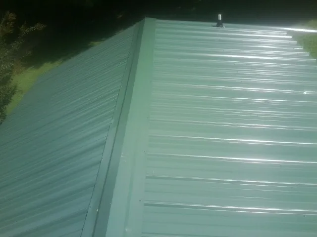 New green metal panels meeting at the ridge of a roof — Flat Roof Repair work by our crew in Slickville