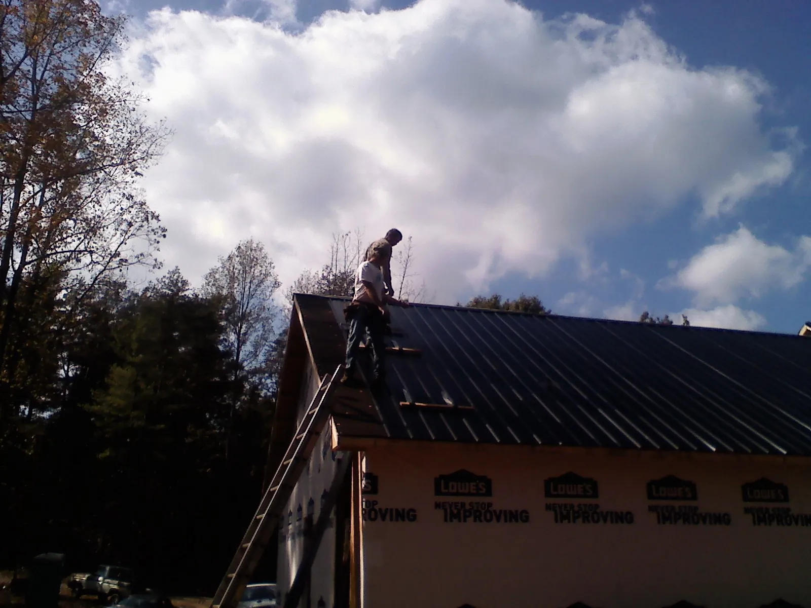Roofer fastening dark metal panels high against a cloudy sky, from a Roof Inspection job in Slickville