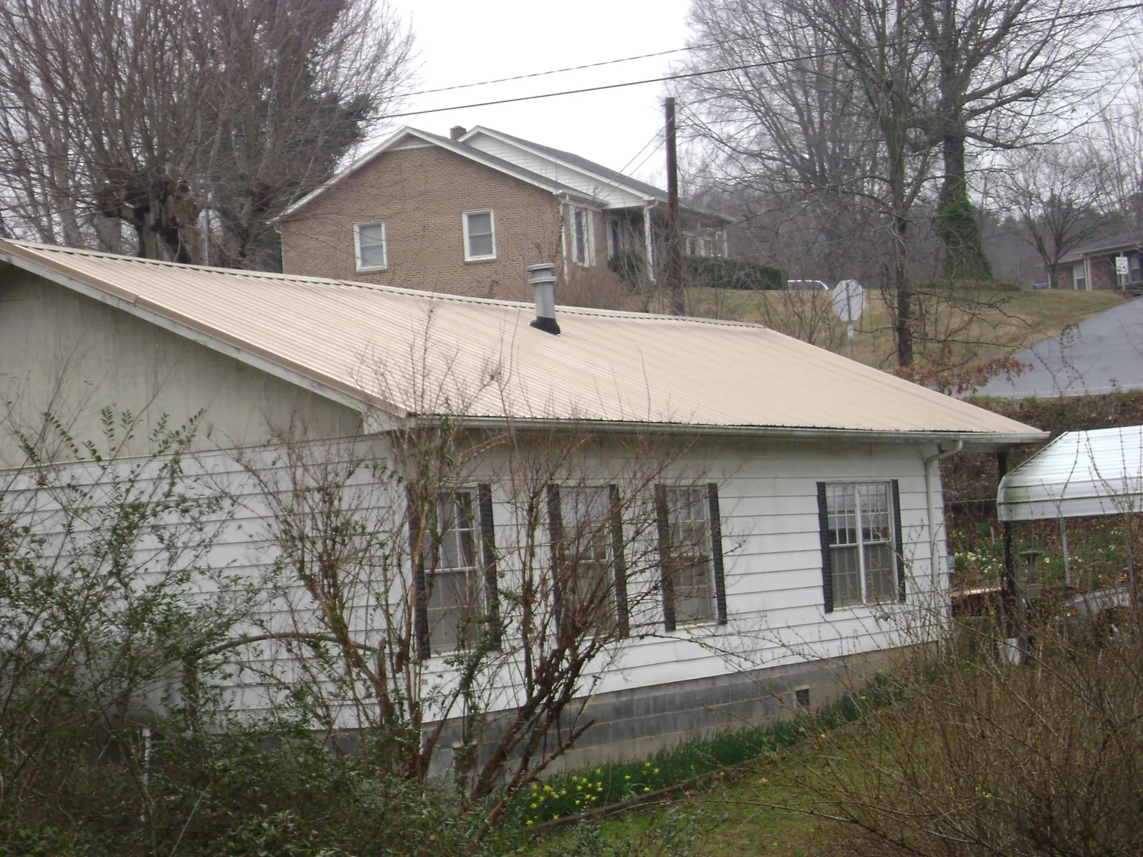 Tan metal roof on a white sided house set into a hillside — Commercial Roofing by Roofing Brothers in Slickville