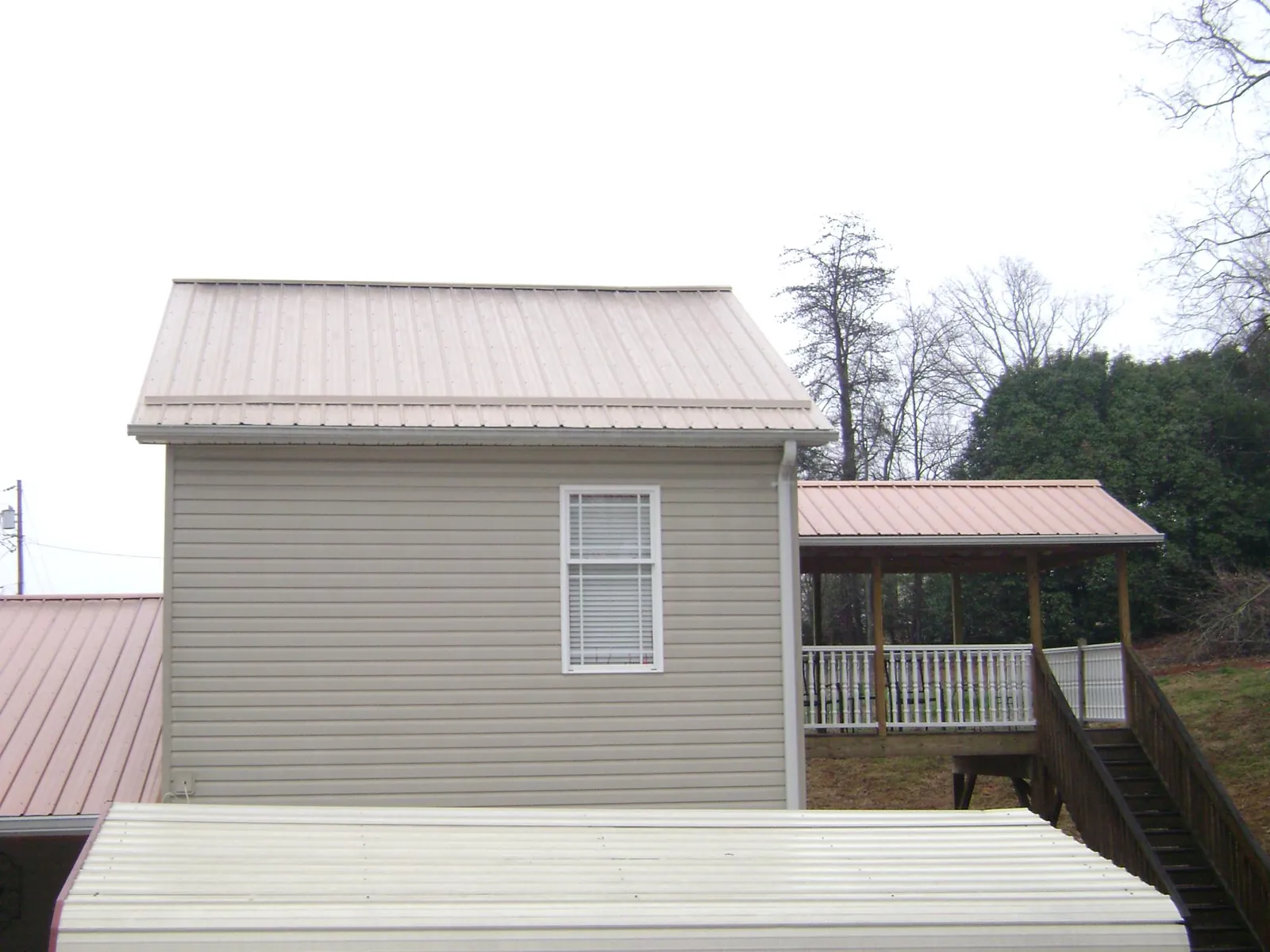 Tan metal roofs on a two story addition and attached porch, from a Roof Replacement job in Slickville